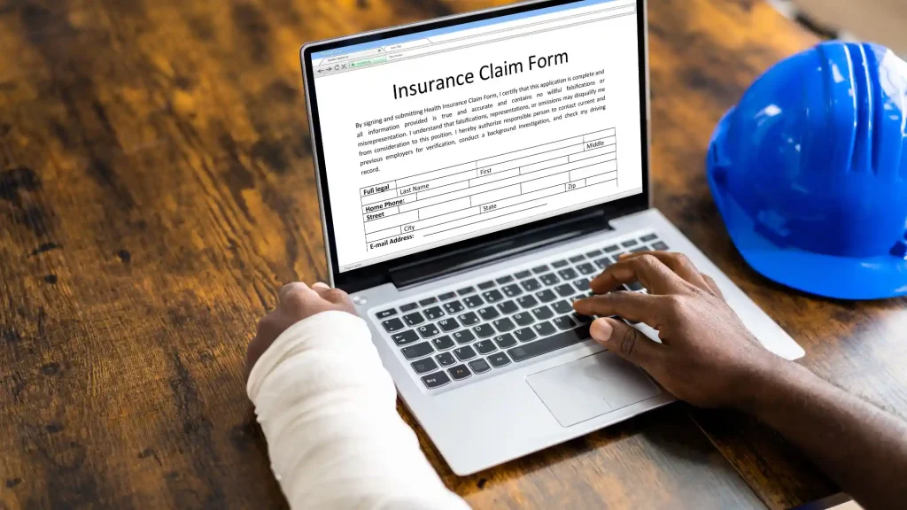 Person with a bandaged arm filling out an insurance claim form on a laptop