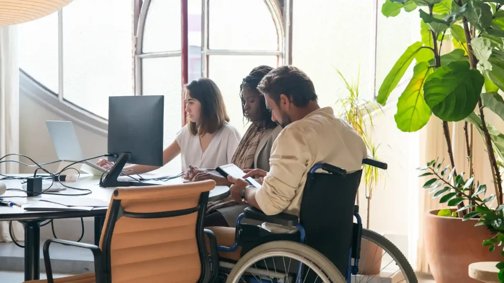Three people collaborating in an office, one sitting in a wheelchair.