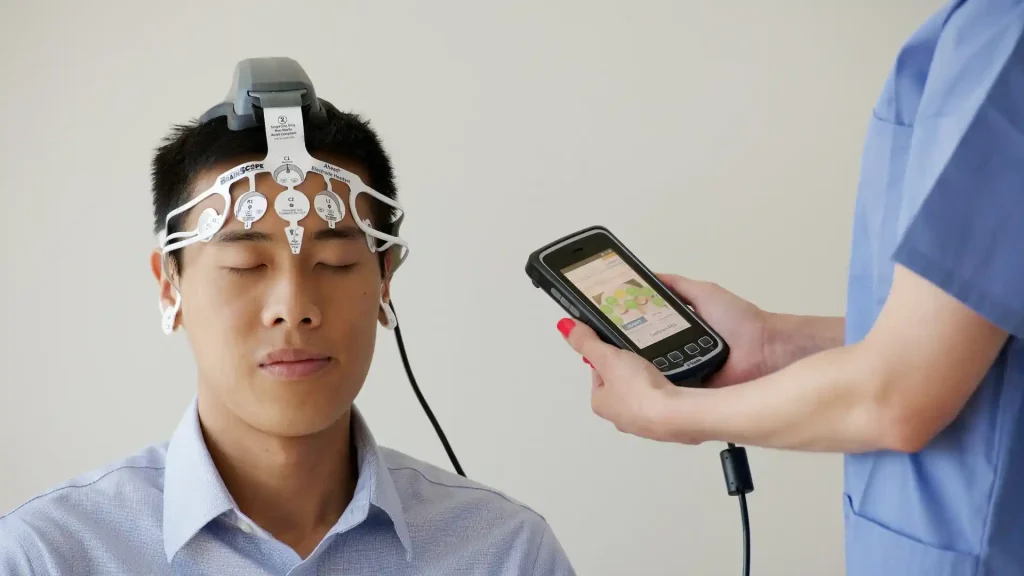 Man wearing EEG electrodes while a technician holds a monitoring device.