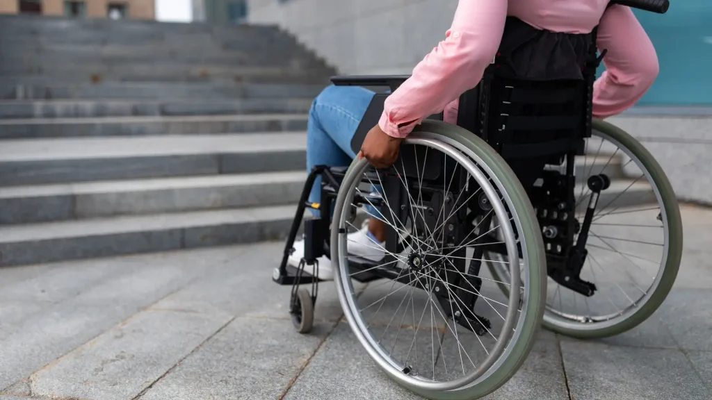 Person pushing a wheelchair up to stairs.
