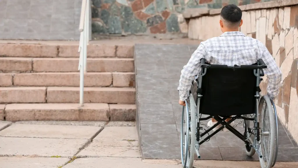 Person in a wheelchair approaching a ramp near stairs.