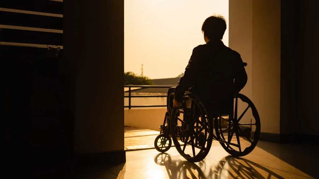 Person sitting in a wheelchair facing the sunset, looking out the door.