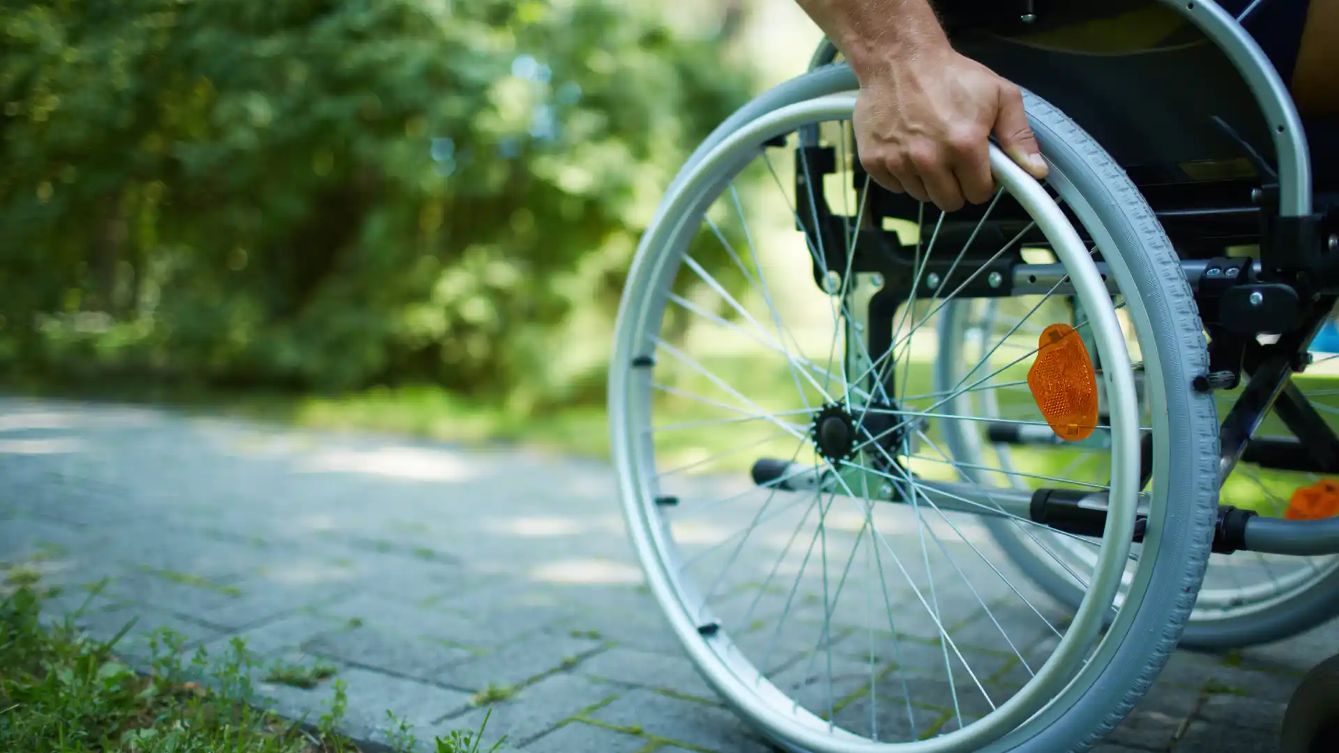 Hand gripping wheelchair wheel for movement outdoors.